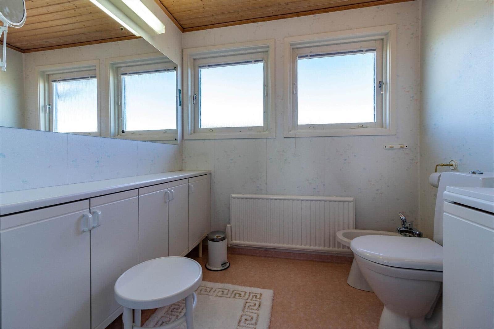 Badezimmer mit Toilette, Bidet und Waschbecken. Drei Fenster und Holzdecke.