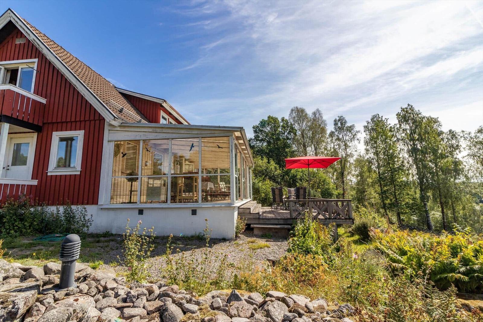 Rotes Haus mit Glasveranda und Terrasse mit rotem Sonnenschirm.