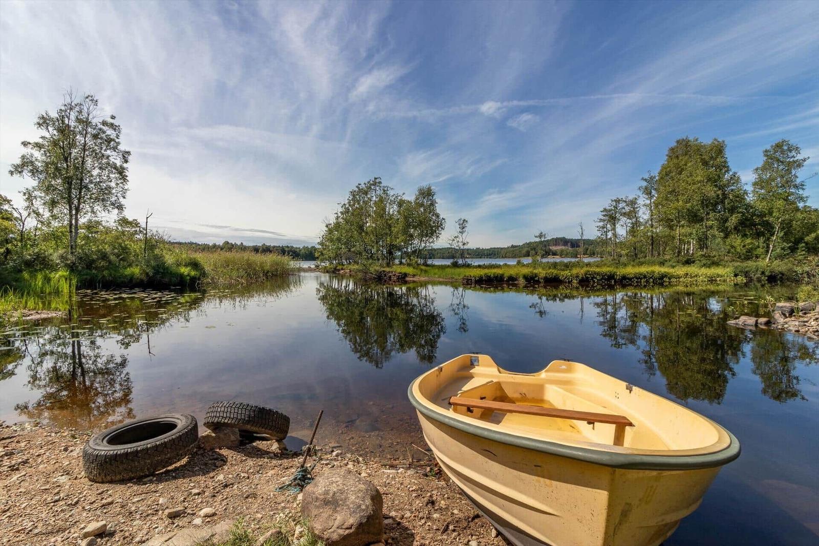 Ein gelbes Boot liegt am Ufer eines ruhigen Sees mit Bäumen und Spiegelungen.