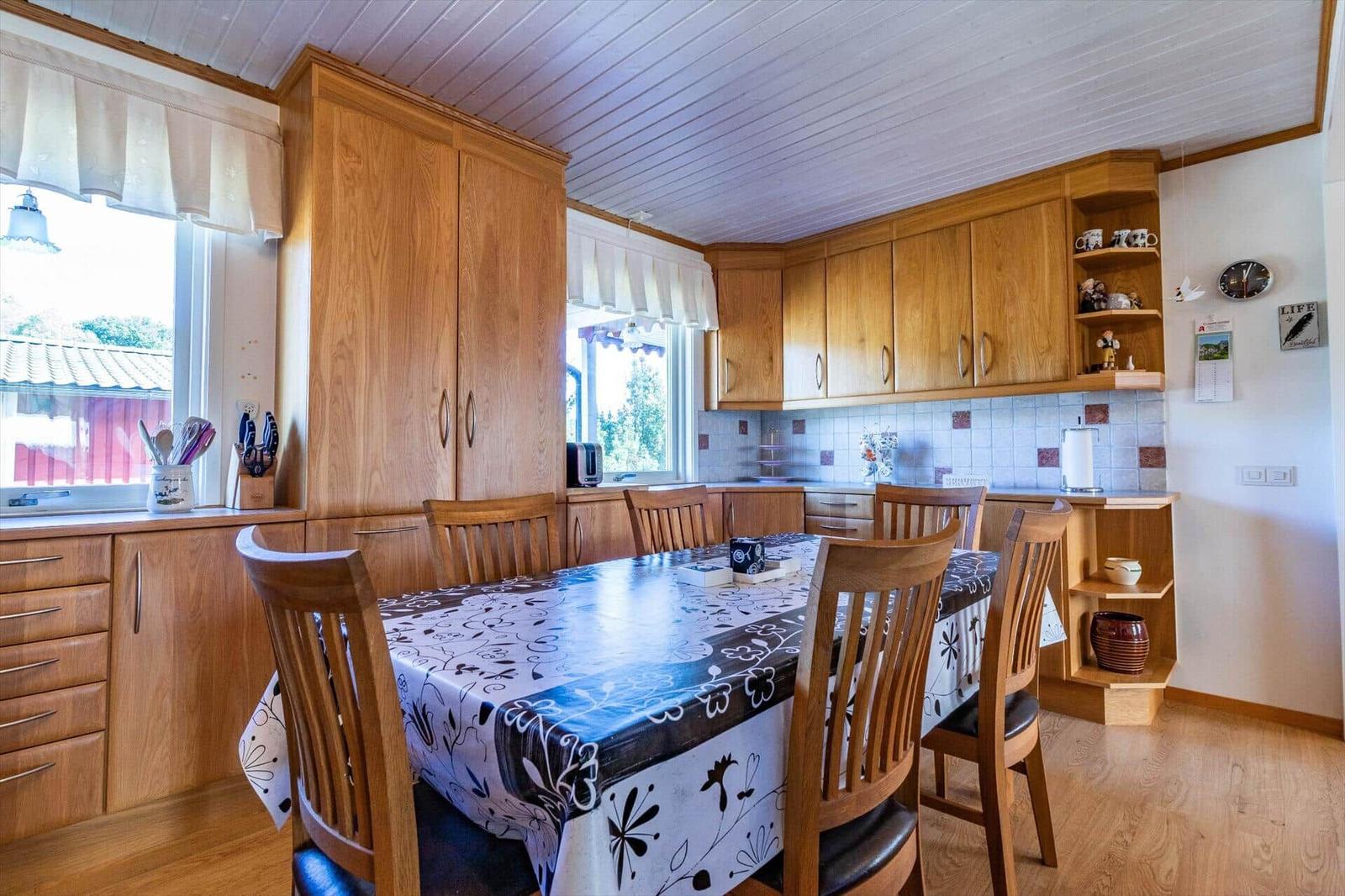 Küche mit Holzmöbeln, Esstisch und Fenstern. Tischdecke mit Blumenmuster.
