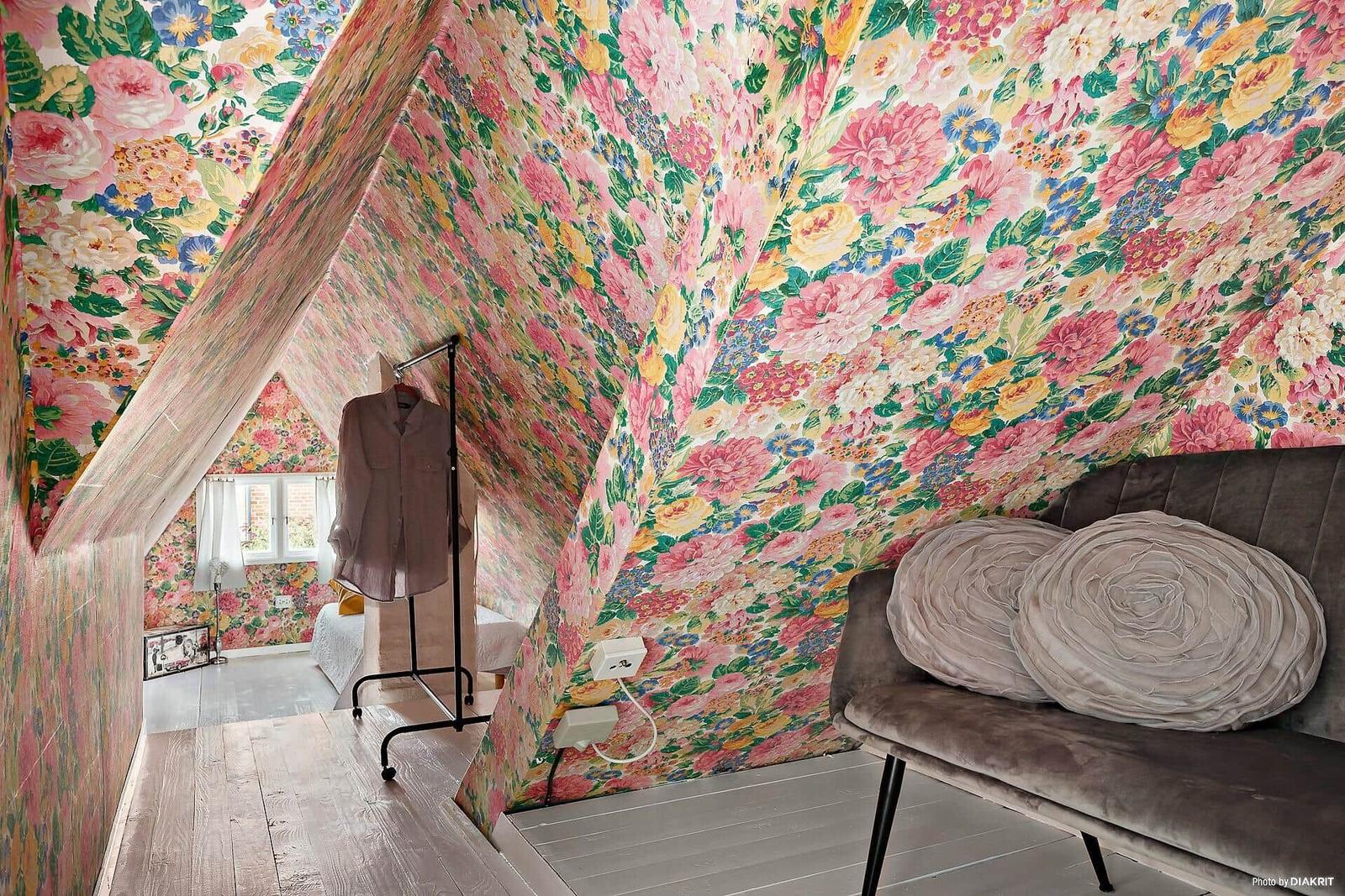 Schlafzimmer mit floraler Tapete, grauer Couch und Kleiderständer.