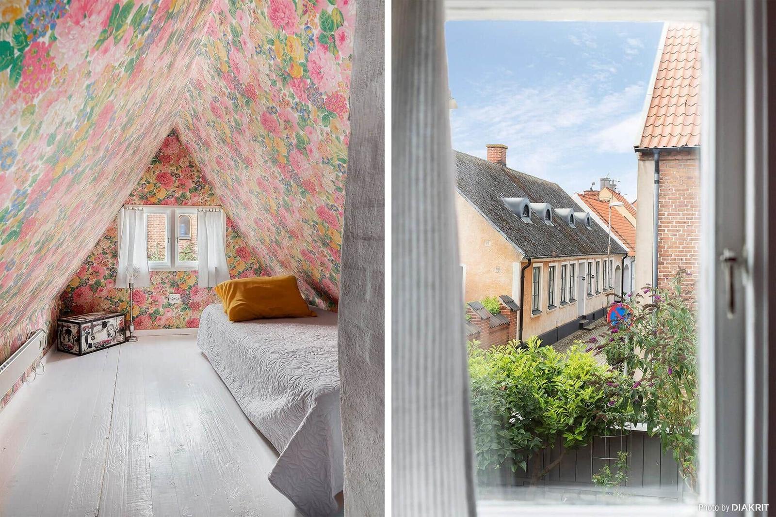 Schlafzimmer mit floraler Tapete und Blick auf eine Straße mit Häusern.