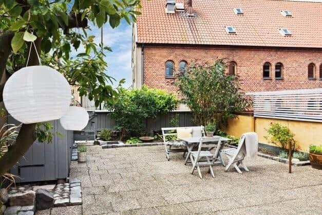 Hinterhof mit Tisch, Stühlen und hängenden Lampen. Im Hintergrund ein Backsteinhaus.