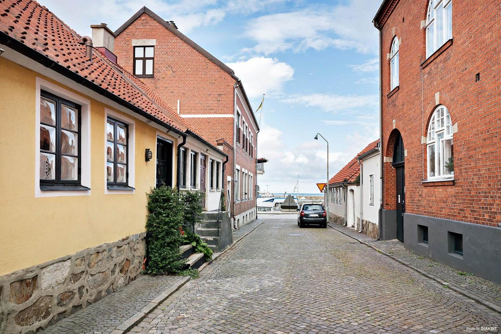 Kurze Straße mit roten Ziegeldächern und Steinmauern führt zum Hafen.