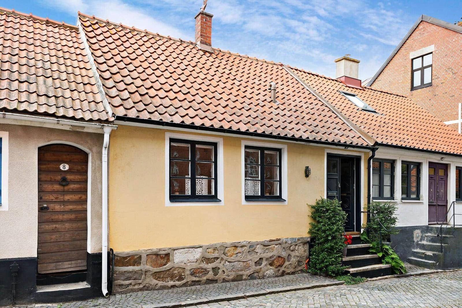 Ein gelbes Haus mit Steinsockel, rotem Ziegeldach und schwarzen Fensterrahmen.