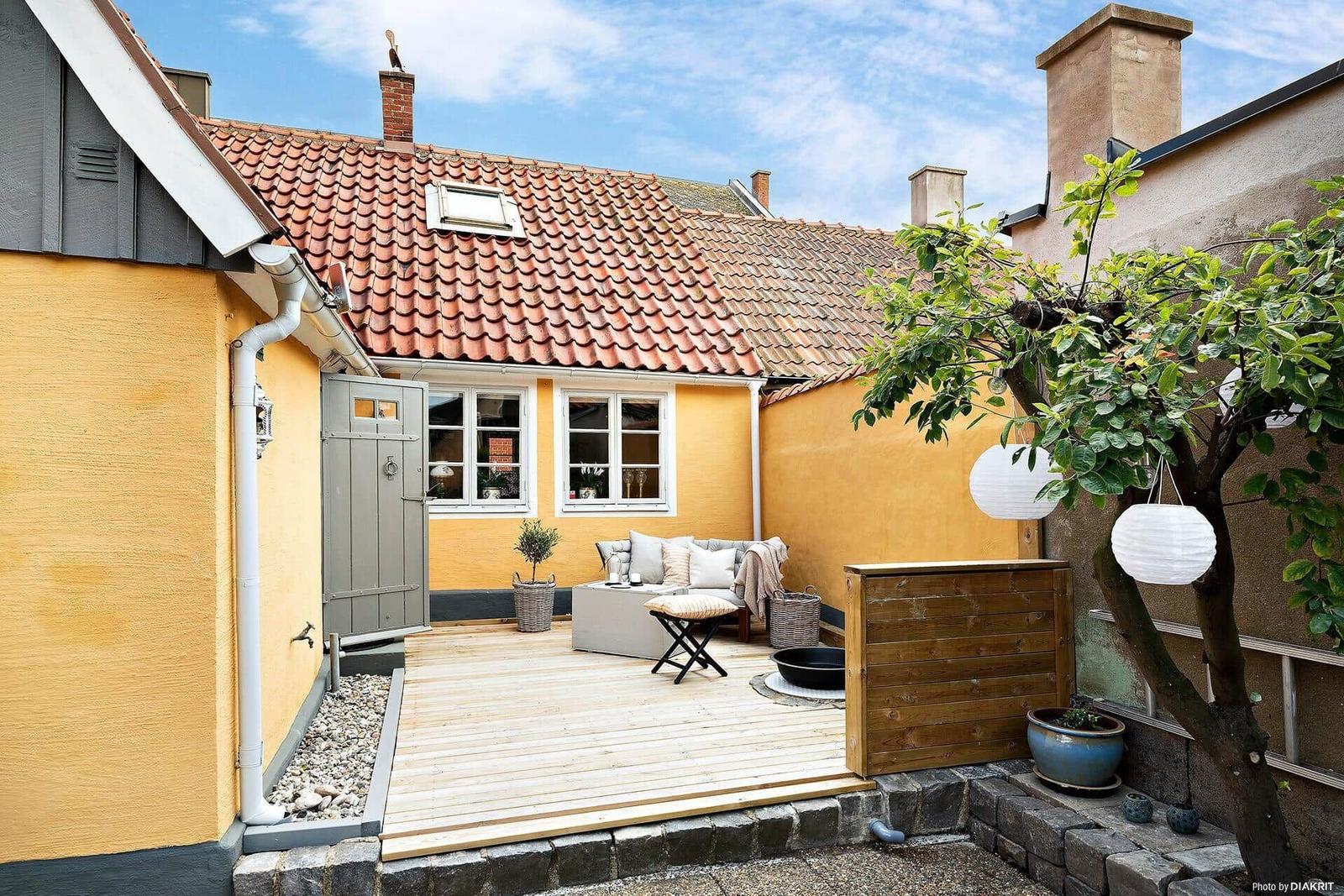 Hinterhof mit Terrasse, Sitzgelegenheit und Baum mit Laternen.
