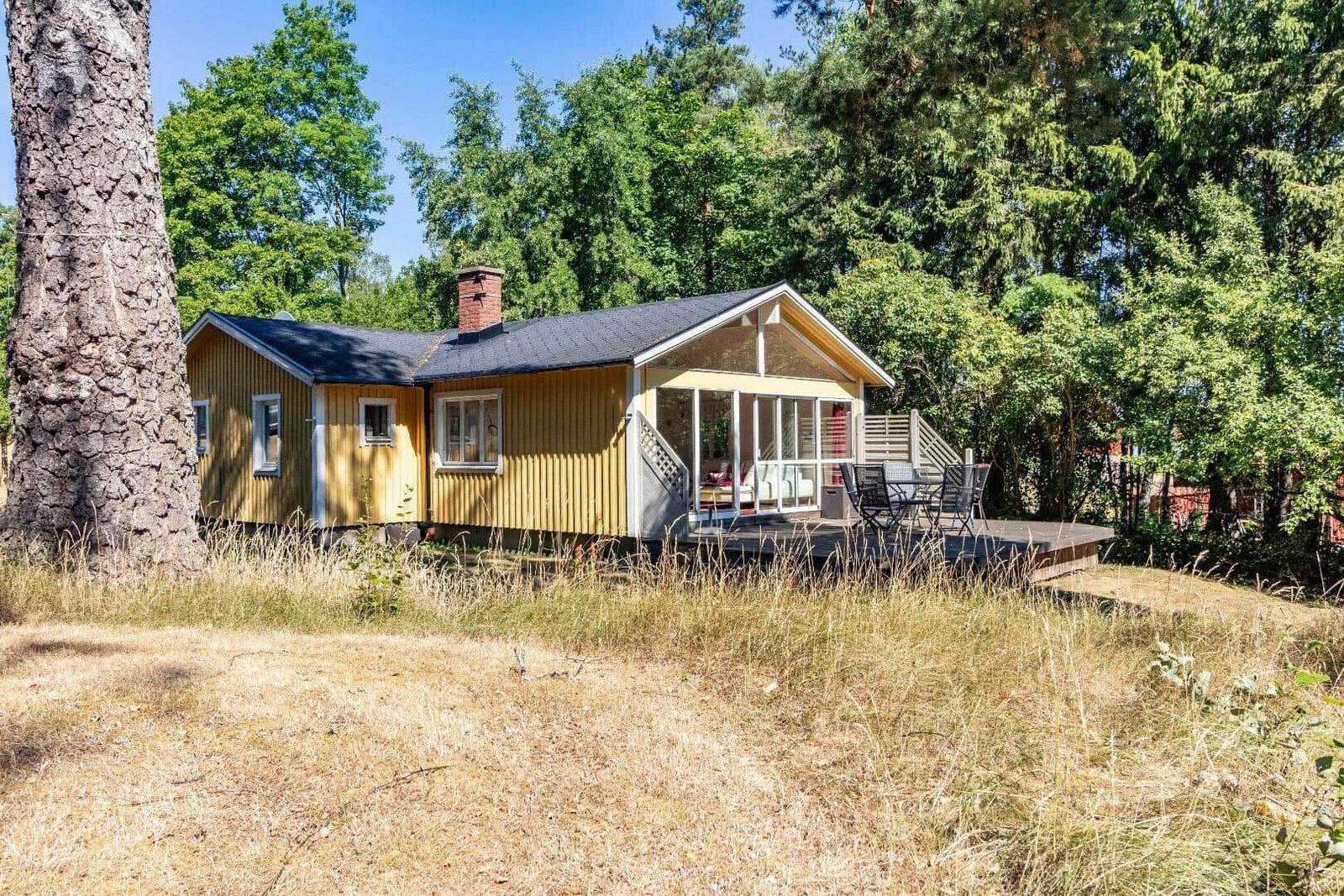 Ein gelbes Holzhaus mit Terrasse und Grillplatz im Wald.