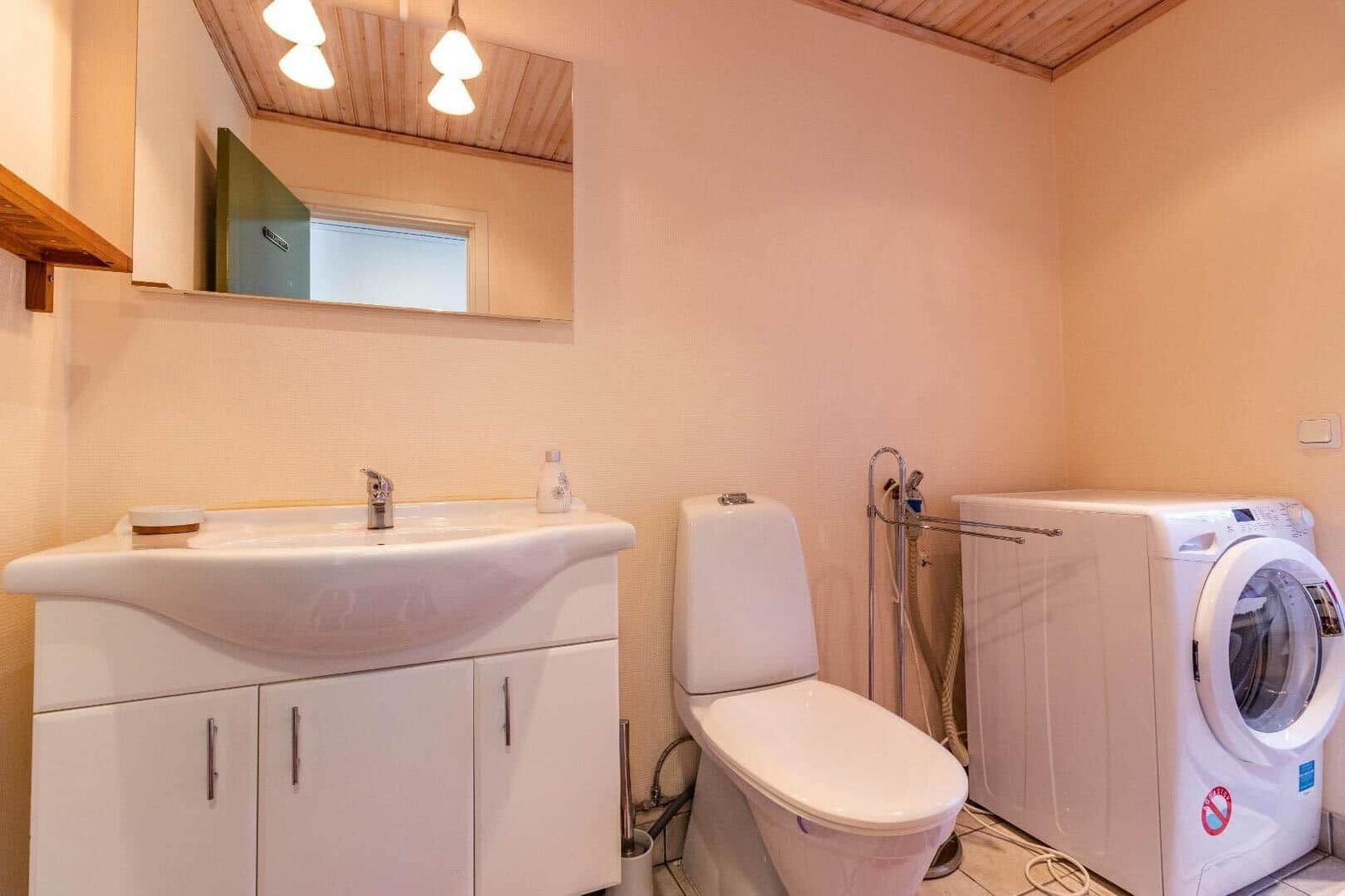 Badezimmer mit Waschmaschine, Toilette und Waschbecken unter Spiegel.