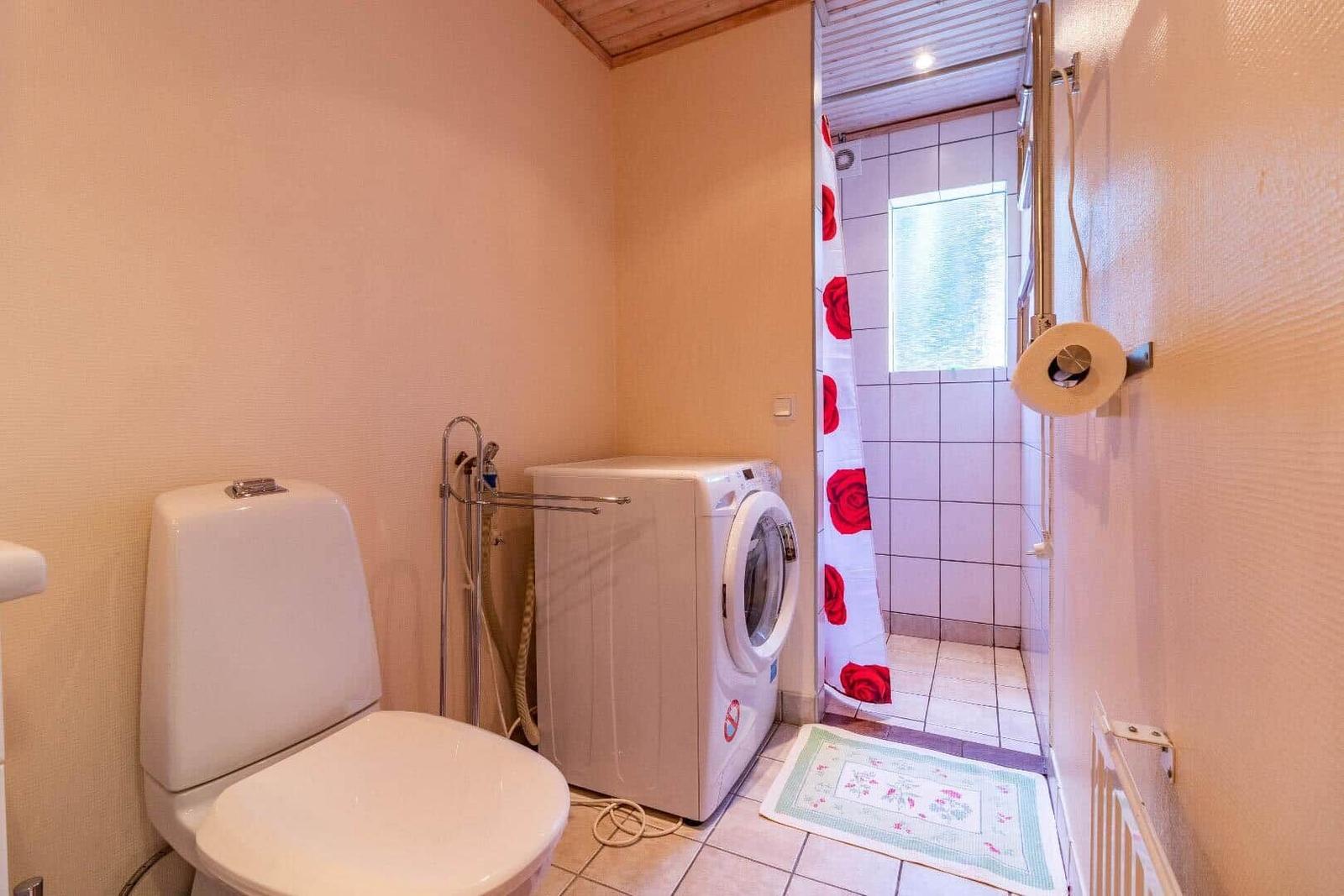 Badezimmer mit Toilette, Waschmaschine und Dusche mit Blumenvorhang.