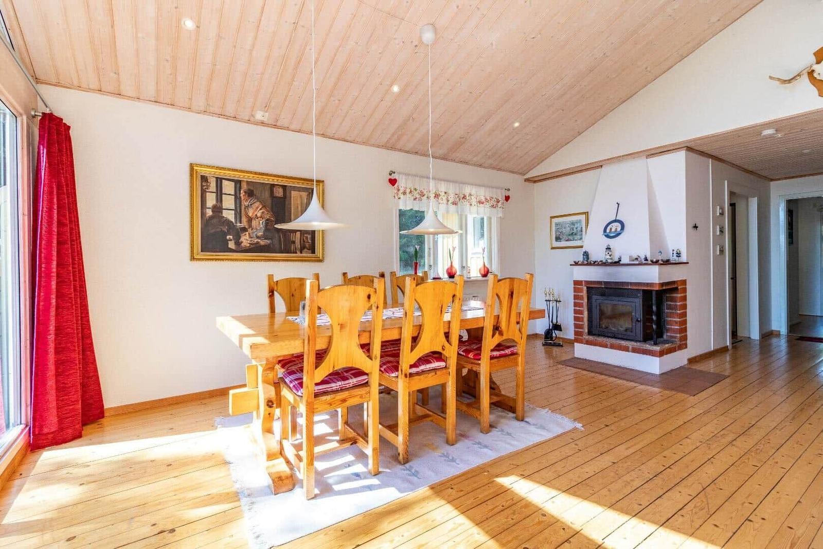 Esszimmer mit Holztisch, Stühlen und Kamin. Holzdecke und -boden. Rote Vorhänge.