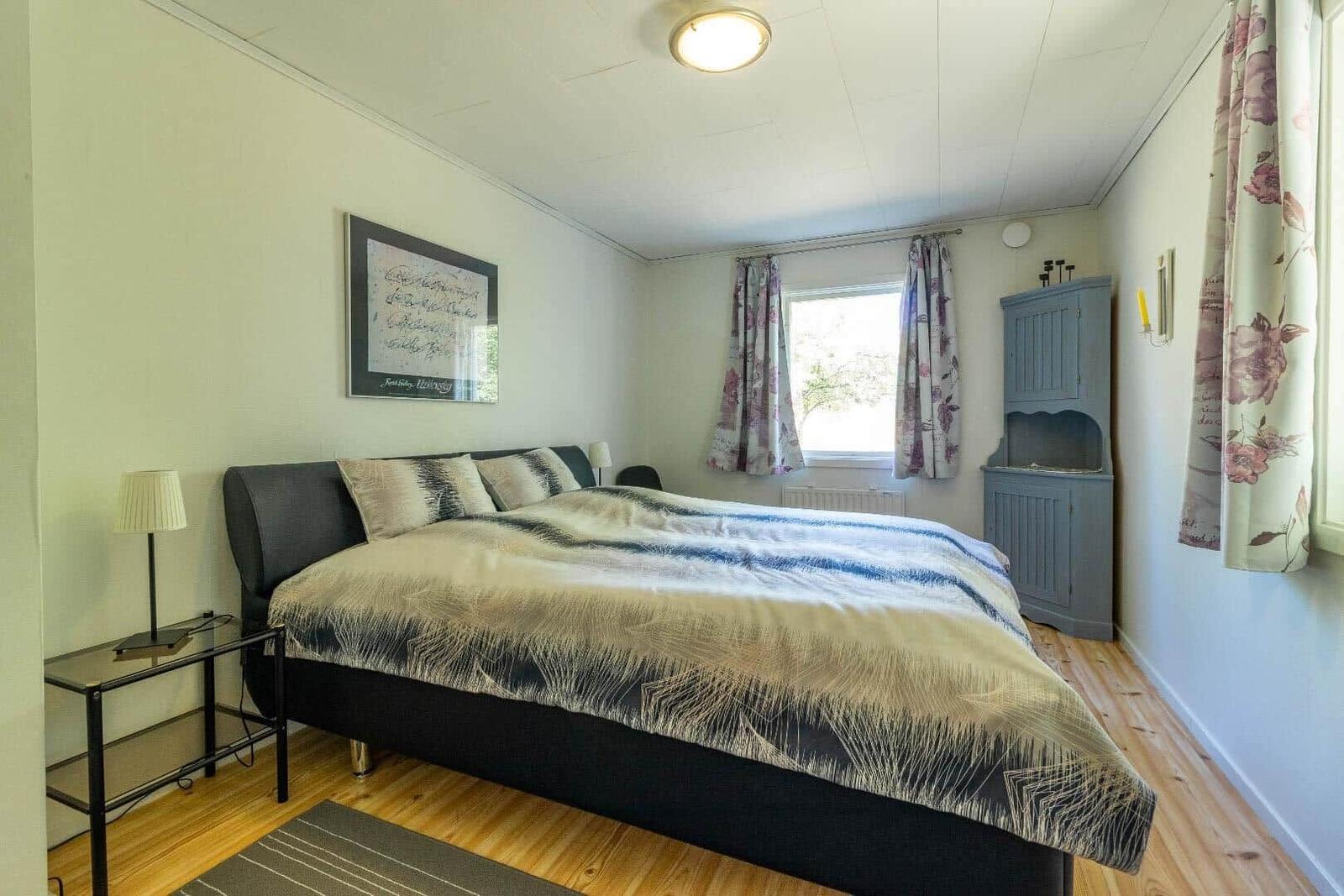 Schlafzimmer mit Bett, Nachttisch, Fenster und blauem Schrank.