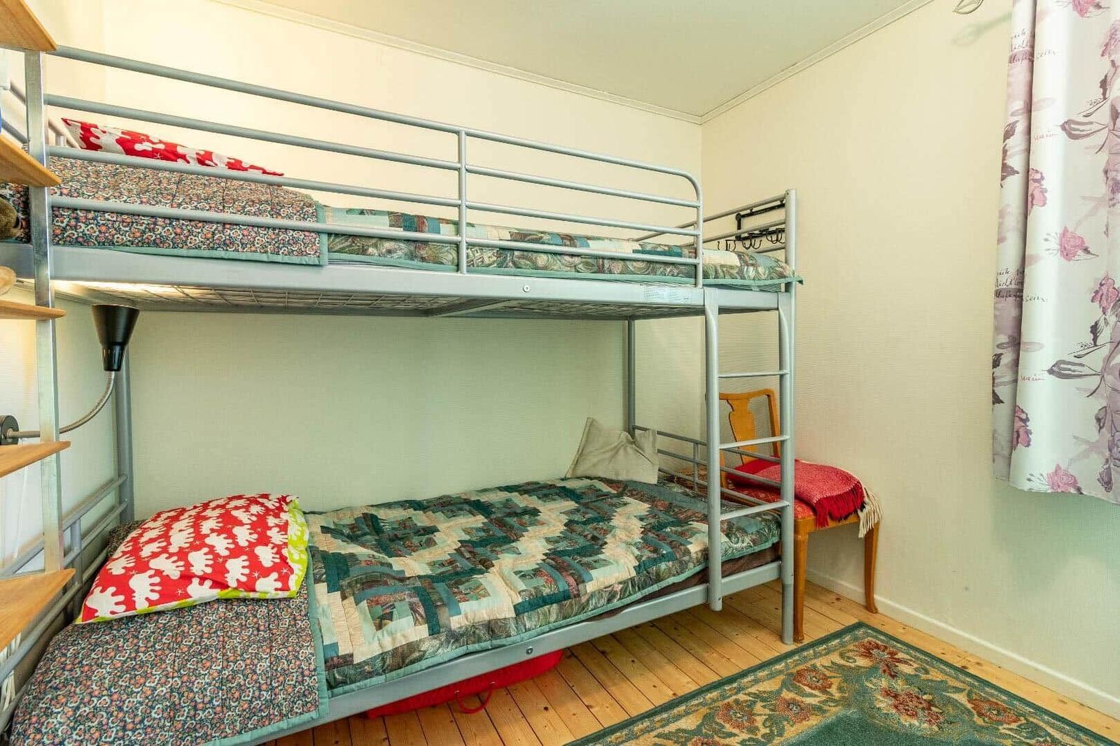 Zimmer mit Doppelstockbett, Holzboden und floraler Gardine.