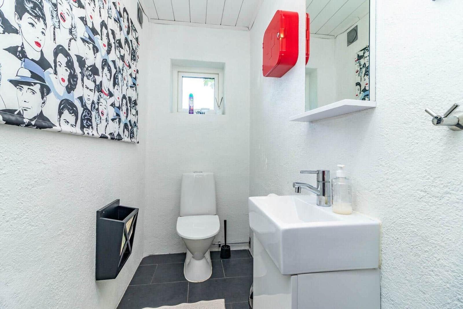 Badezimmer mit Toilette, Waschbecken und Wandbild mit Porträts.