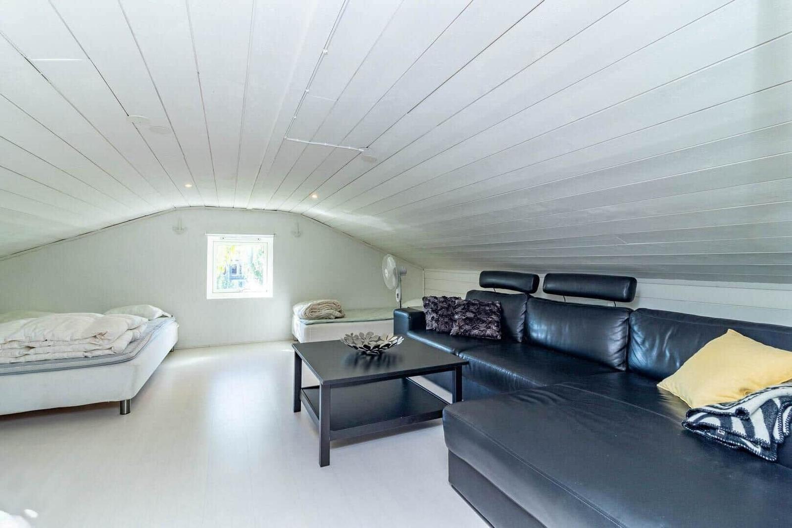 Ein Raum mit schwarzem Sofa, weißem Bett und schrägem Dach mit Fenster.