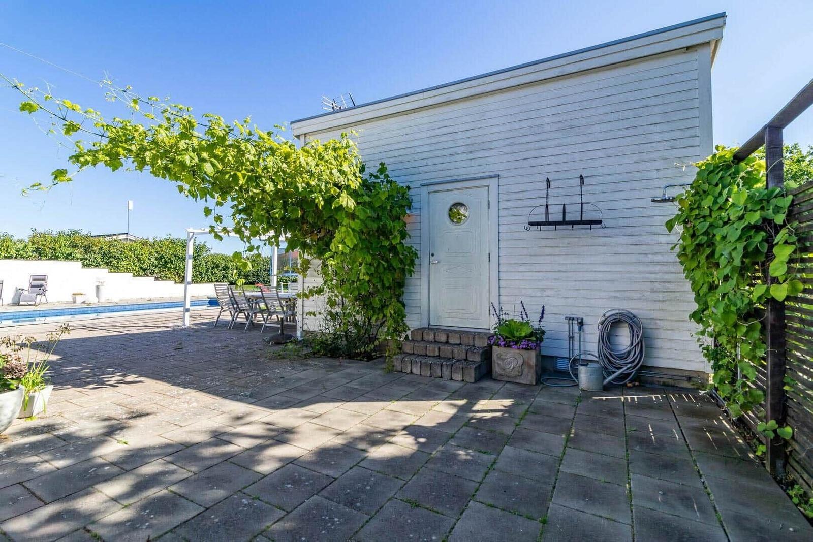 Haus mit Terrasse, Pool und Pflanzen. Tür mit Rundfenster und Gartengeräte.