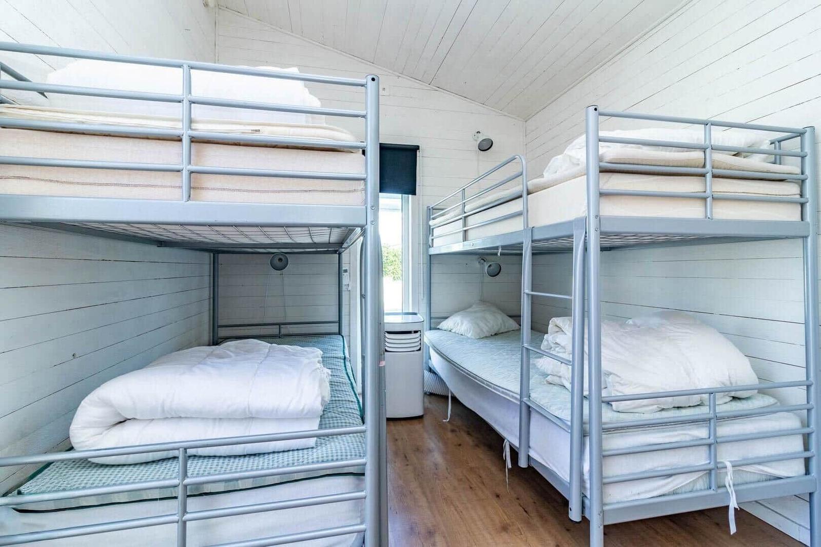 Zwei Etagenbetten mit Matratzen und Bettwäsche in einem Raum mit Holzboden und weißem Holzverkleidung.