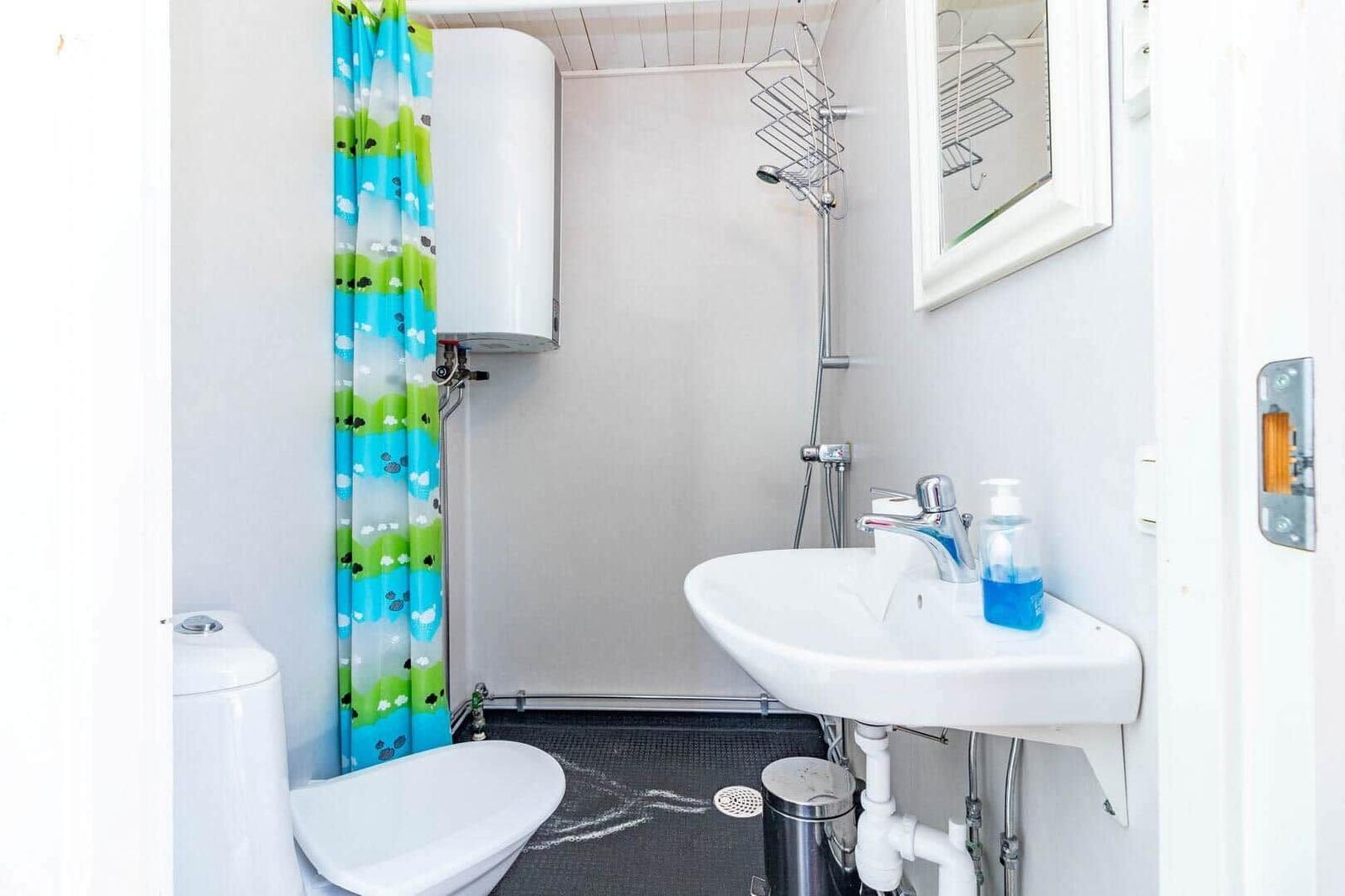 Badezimmer mit Dusche, Waschbecken und Toilette. Farbiger Duschvorhang und Spiegel.