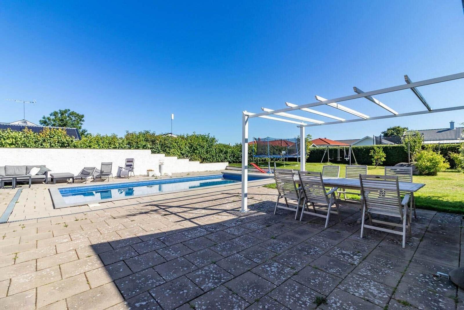 Poolbereich mit Sitzgelegenheiten und Pavillon. Hintergrund mit Grün und Haus.