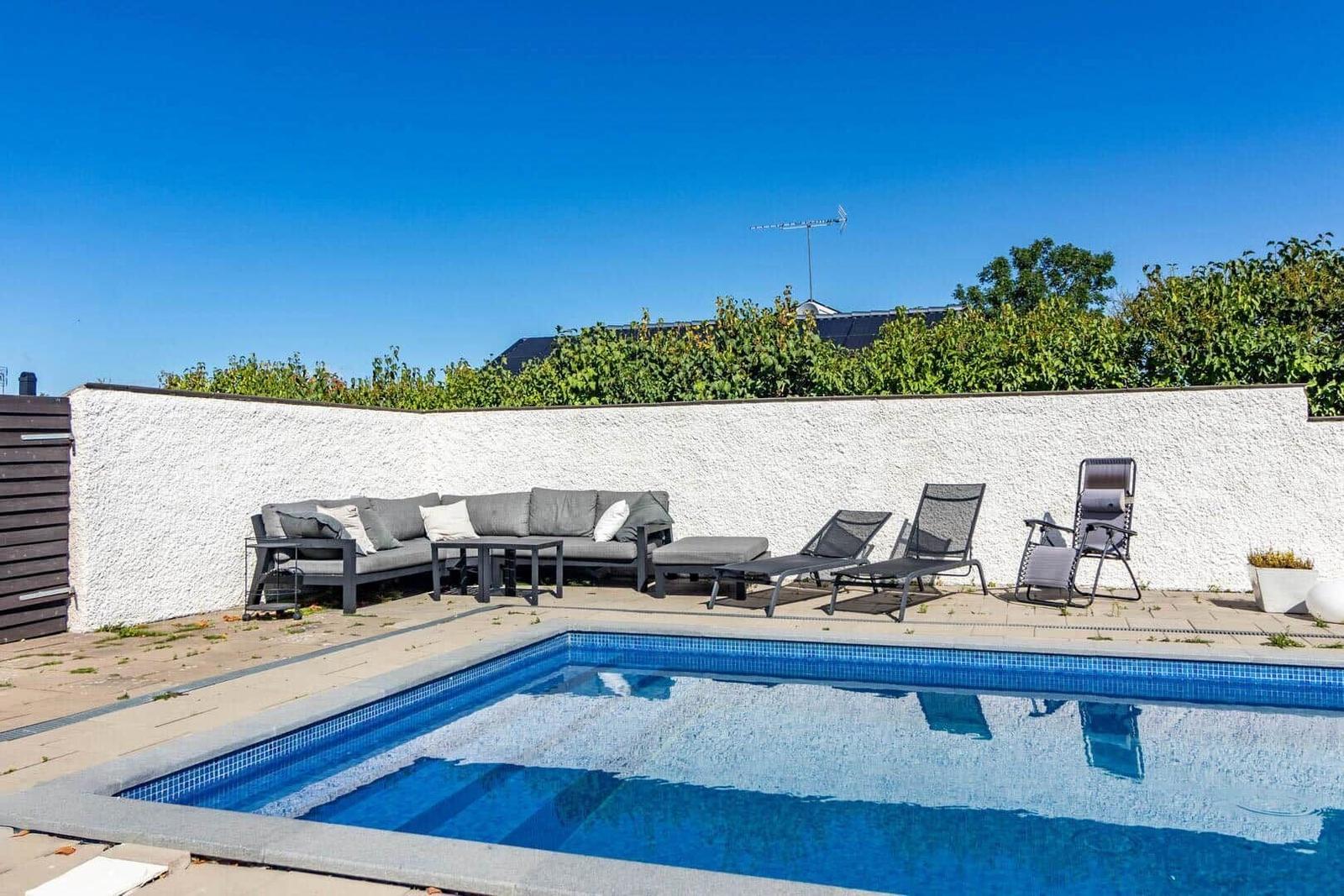 Poolbereich mit Sitzgruppe und Liegestühlen an weißer Wand.