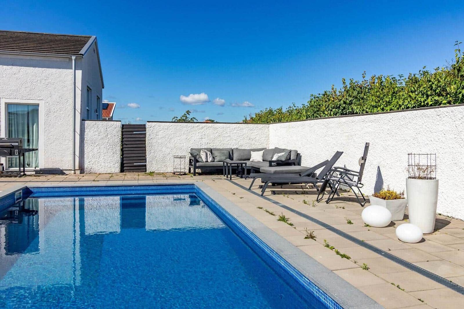 Poolbereich mit Loungemöbeln und weißen Wänden unter blauem Himmel.