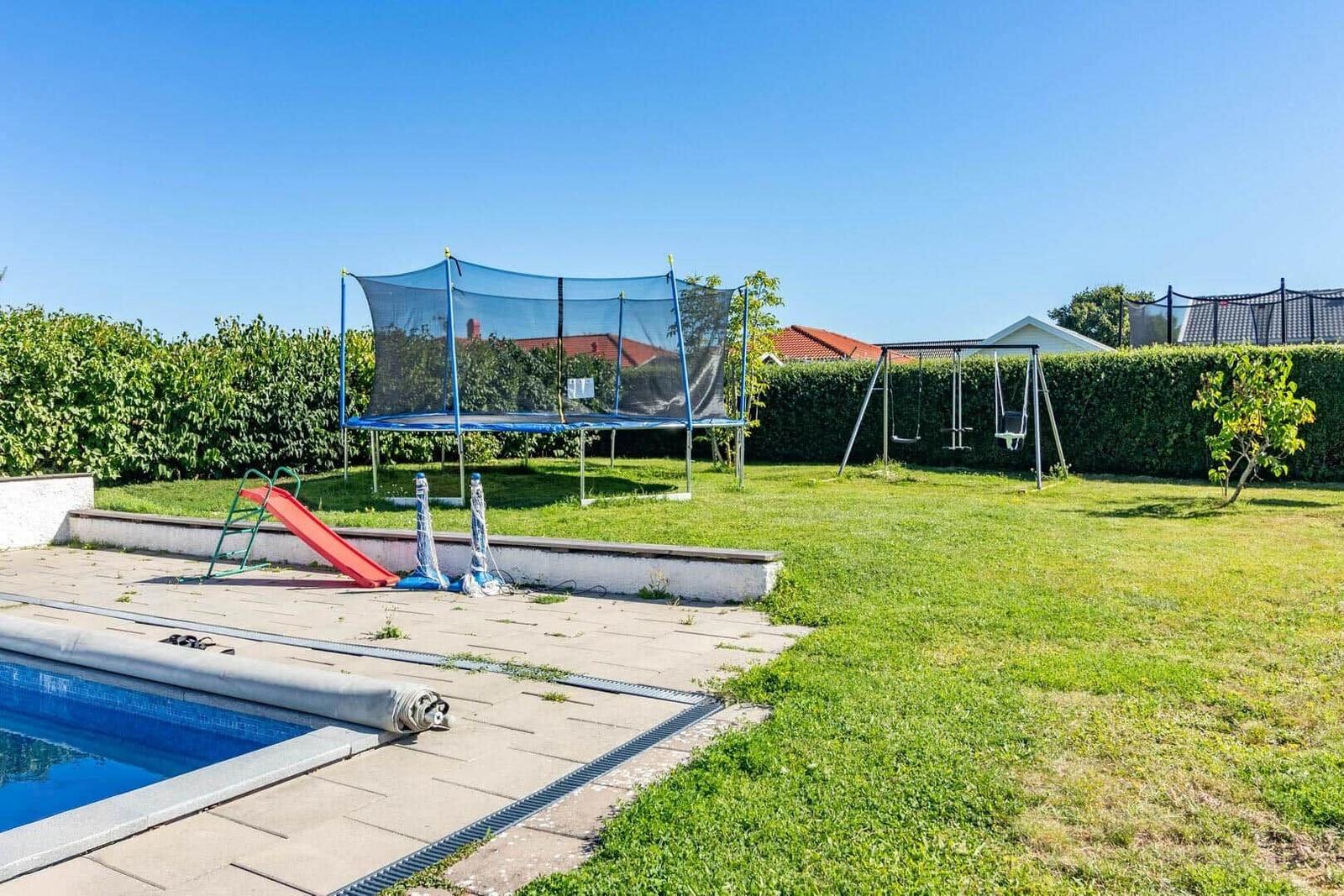 Poolbereich mit Trampolin, Rutsche und Schaukel im Garten.