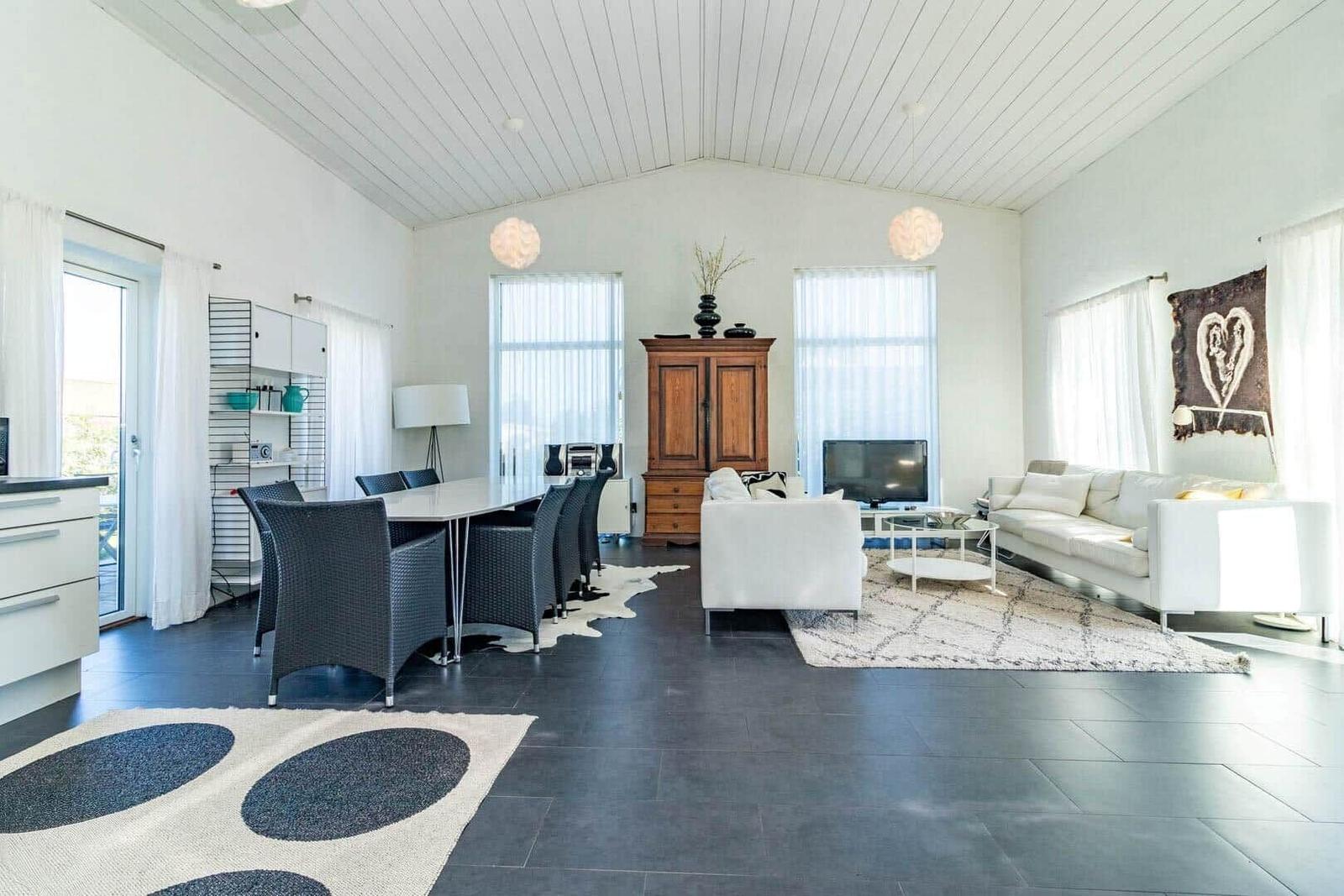 Großer Wohnbereich mit Essbereich, weißen Sofas, Holzschrank und dunklem Boden.