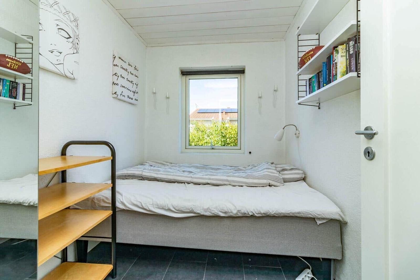 Schlafzimmer mit Bett, Fenster, Wandregalen und Schreibtisch.