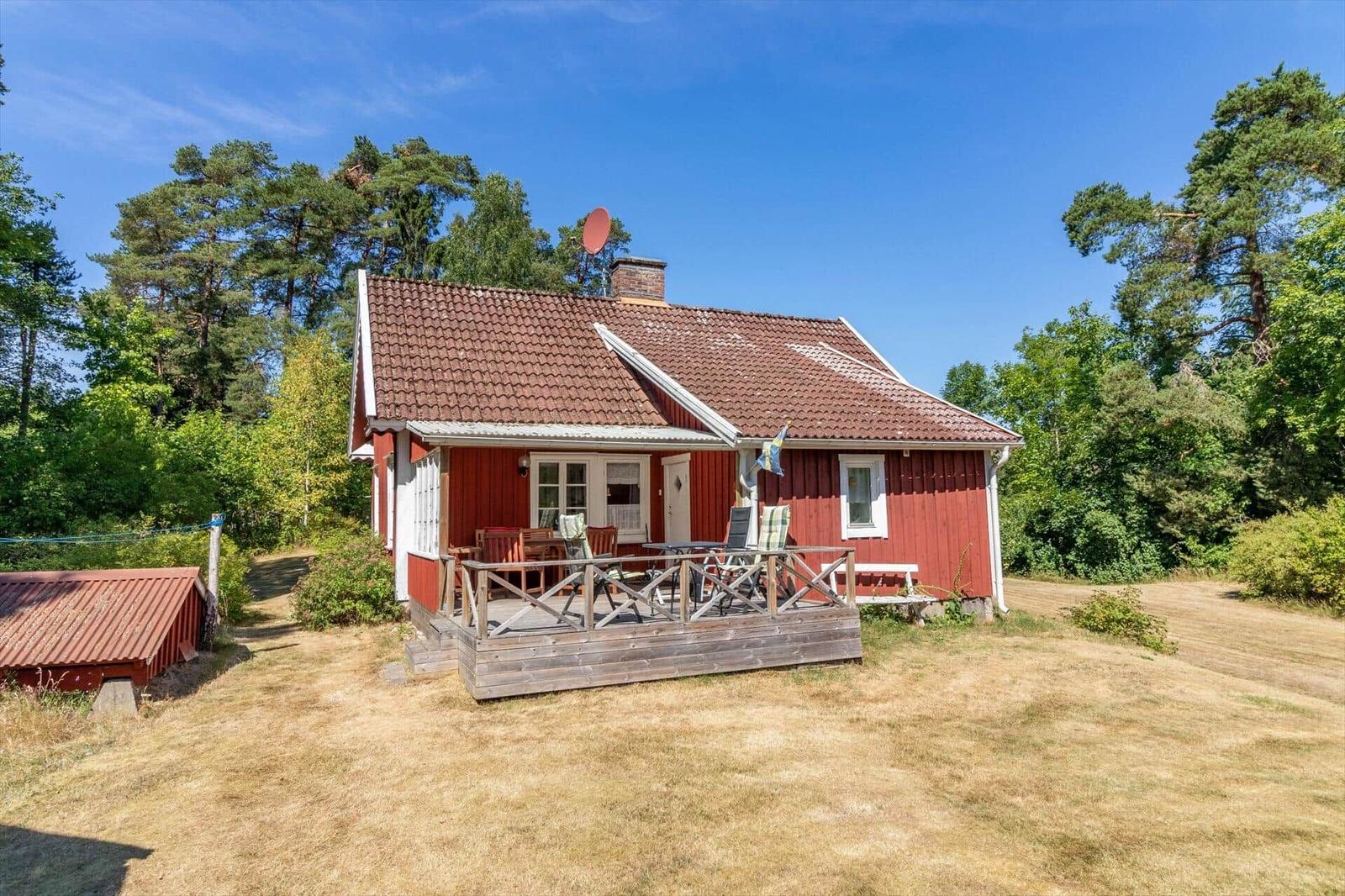 Rotes Holzhaus mit Terrasse, Garten und Wald im Hintergrund.