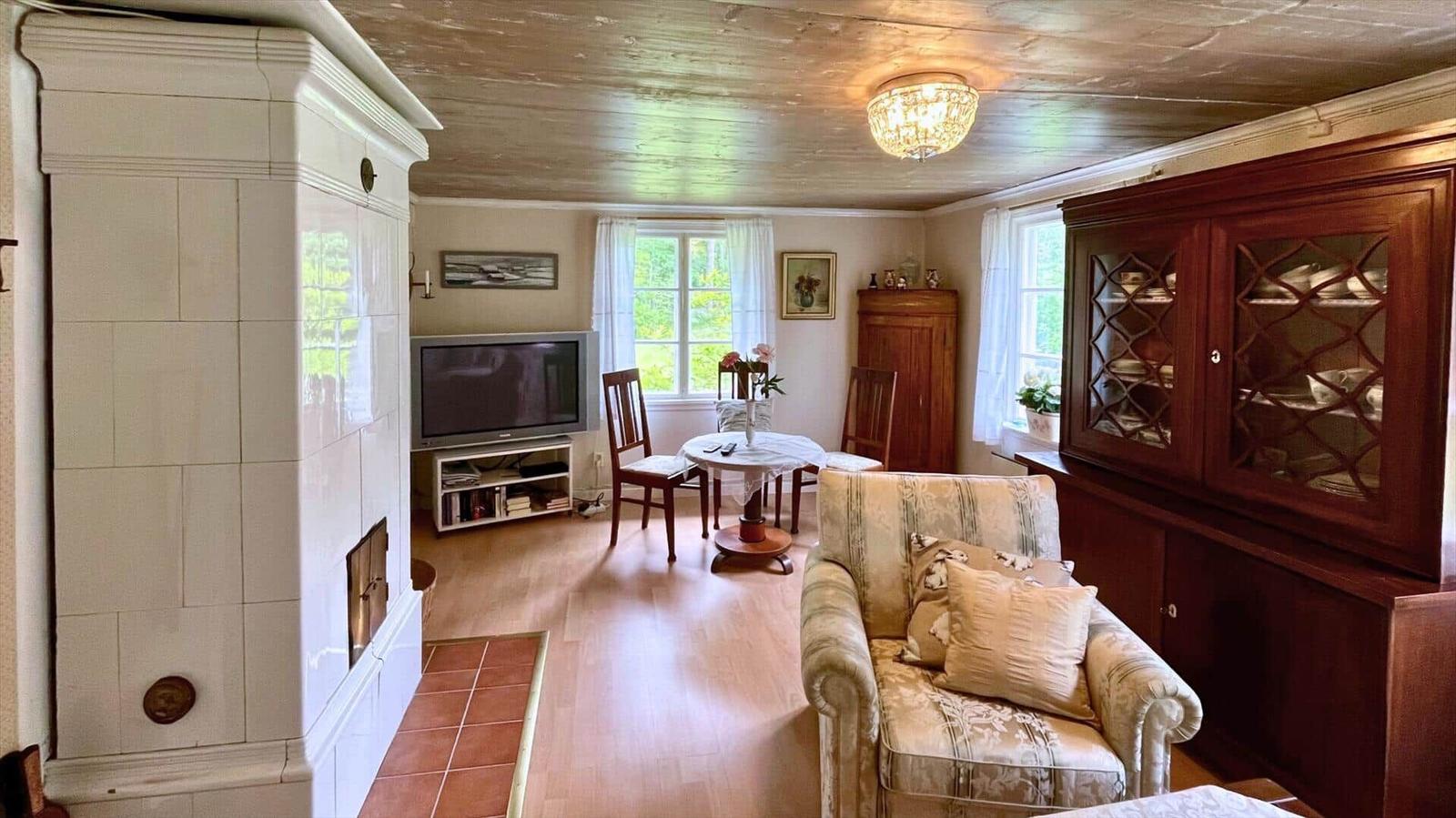 Wohnzimmer mit Kamin, TV, Esstisch und Holzmöbel. Holzdecke und Fenster mit Blick ins Grüne.