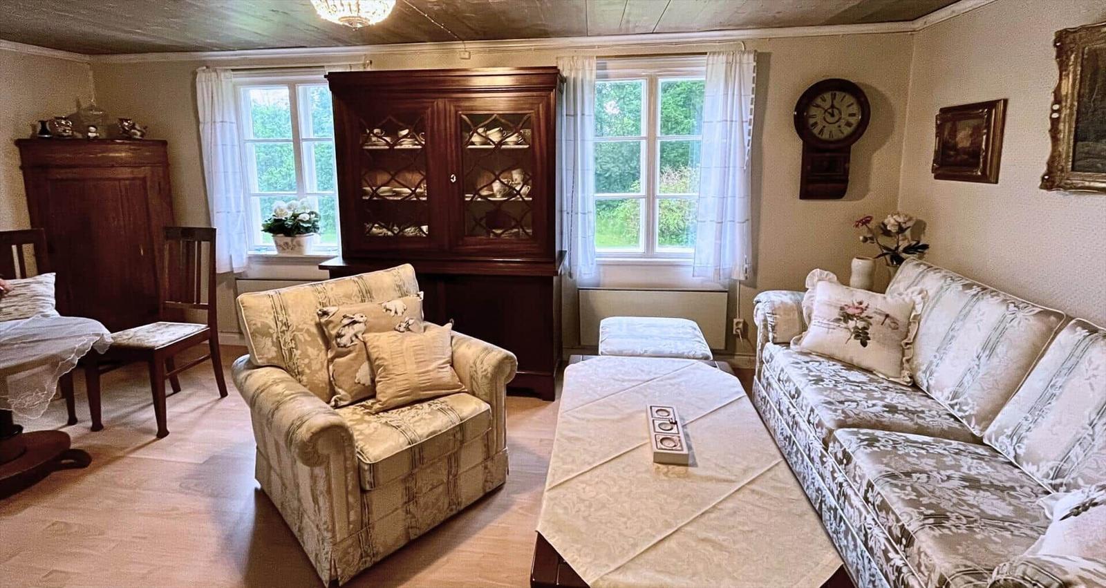 Wohnzimmer mit Sofa, Sessel, Couchtisch und Holzmöbel. Fenster mit Blick auf Grün.