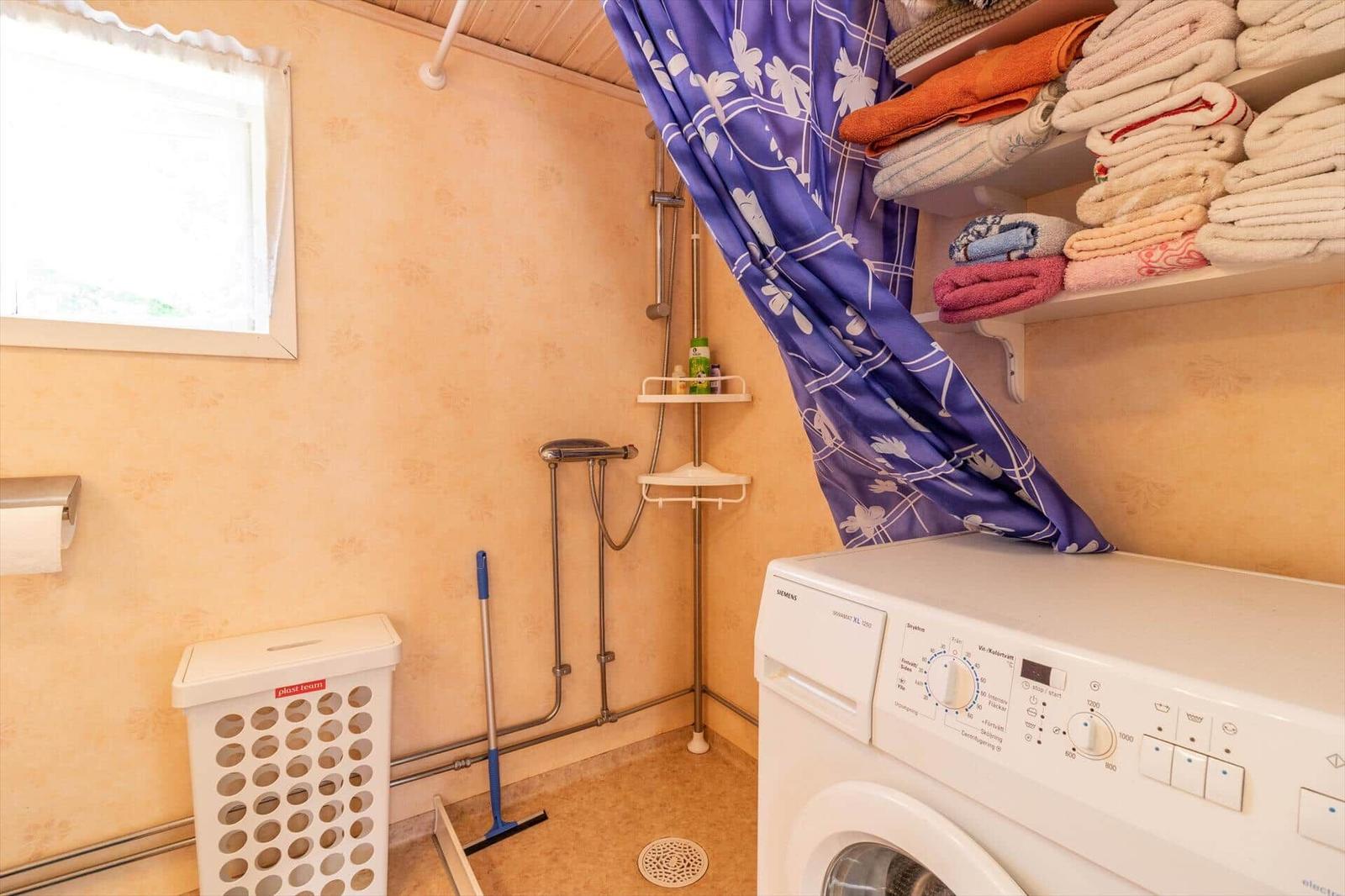 Badezimmer mit Dusche, Waschmaschine und Regalen für Handtücher.