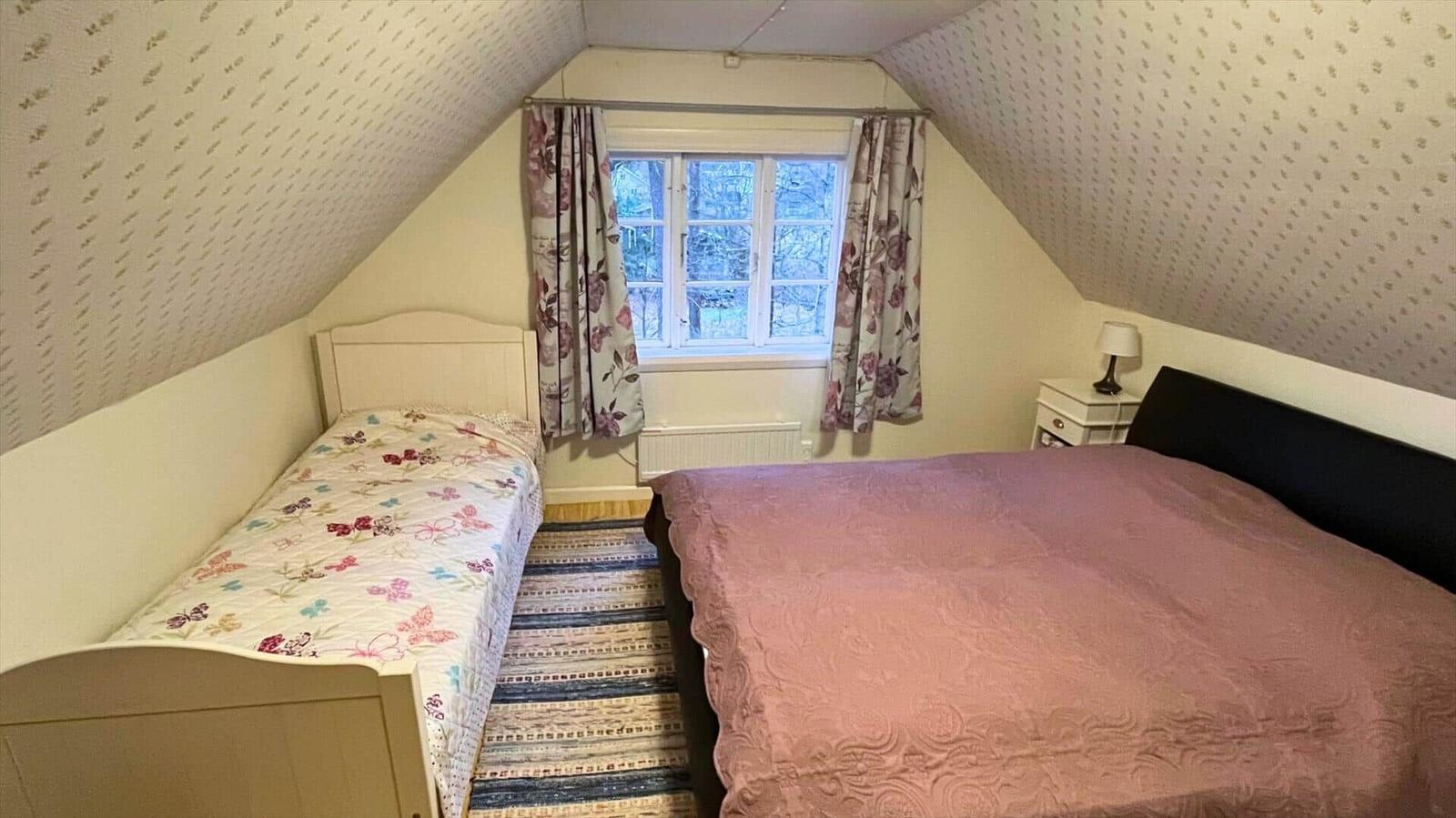 Zimmer mit zwei Betten, Fenster mit Vorhängen und schrägen Wänden.