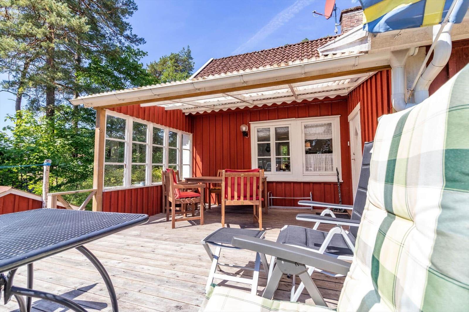 Roter Holzhaus mit Terrasse, Gartenmöbel und Blick in den Wald.