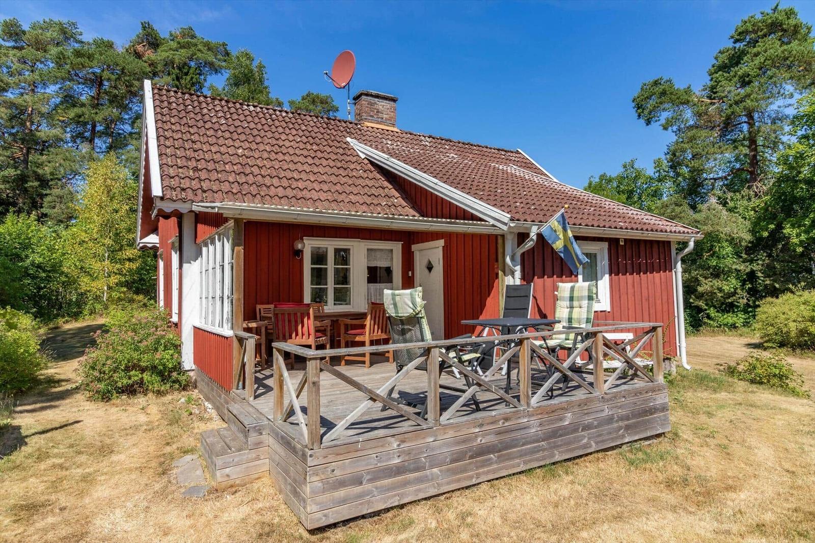 Rotes Holzhaus mit Terrasse, Garten und schwedischer Flagge.