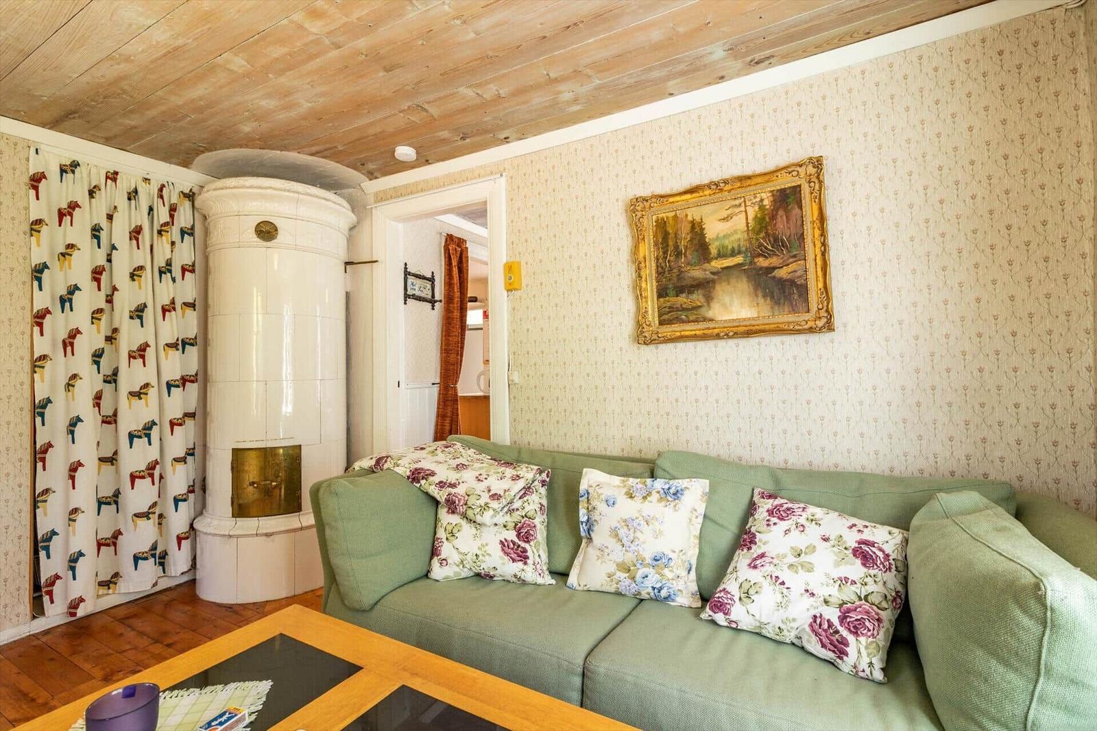 Ein Wohnzimmer mit grünem Sofa, floralen Kissen und einem weißen Ofen.