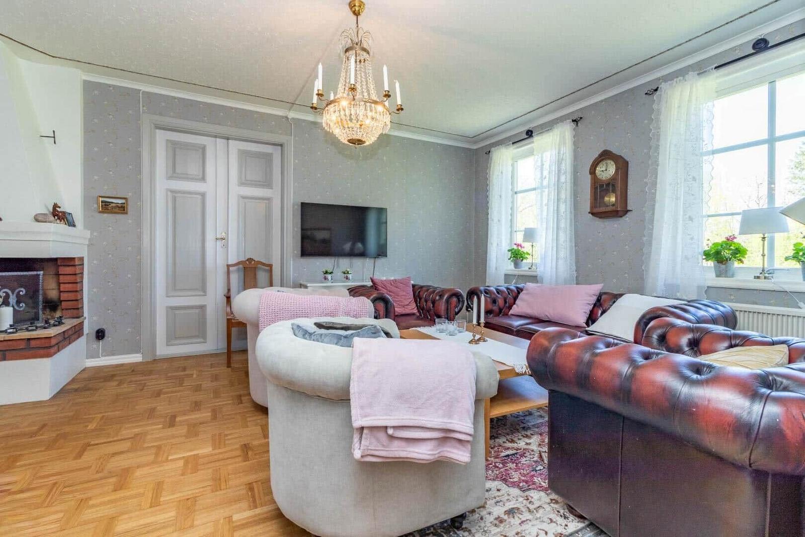 Wohnzimmer mit Ledersofa, Kamin und Kronleuchter. Holzboden und große Fenster.