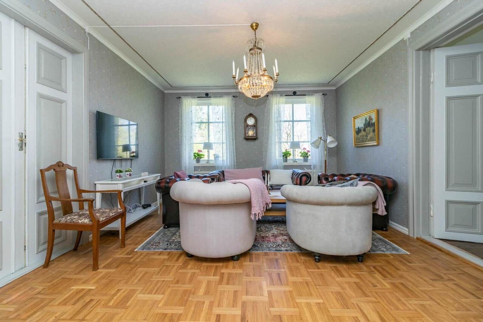 Wohnzimmer mit zwei runden Sesseln, Ledersofa, Holzboden und Kronleuchter.