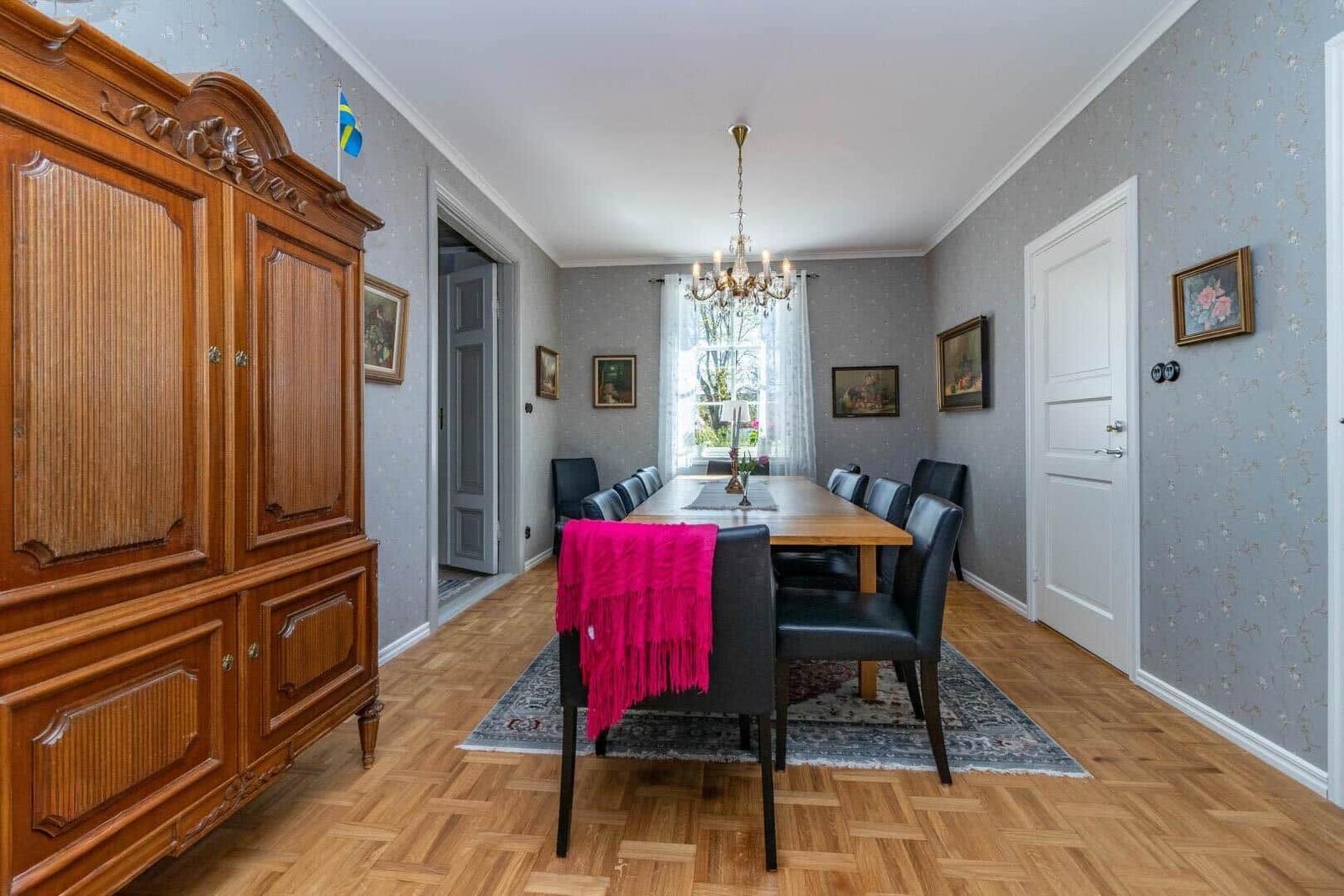 Esszimmer mit Holzboden, Esstisch, Stühlen und Kronleuchter. An der Wand hängen Bilder.