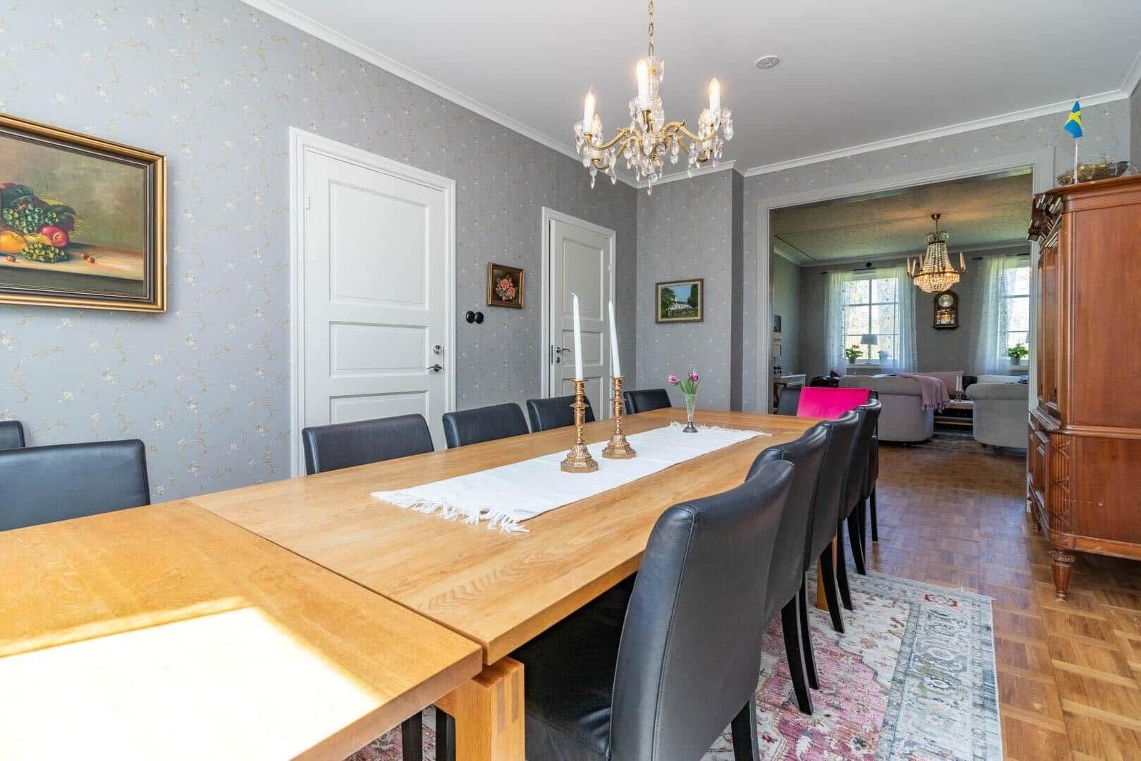 Esszimmer mit Holztisch, schwarzen Stühlen und Kronleuchter. Wohnzimmer im Hintergrund.