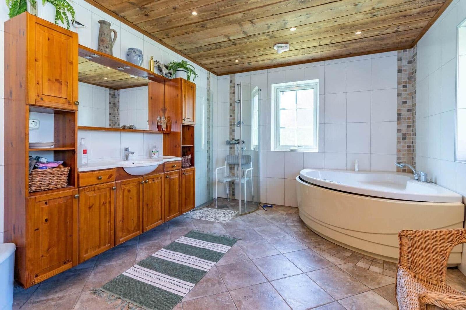 Bad mit Holzdecke, Badewanne, Dusche und Waschbecken mit Holzschrank.
