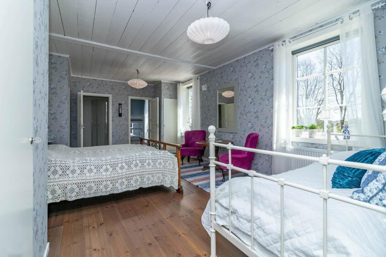 Zimmer mit zwei Betten, Fenster, Wandtapete und Stühlen.