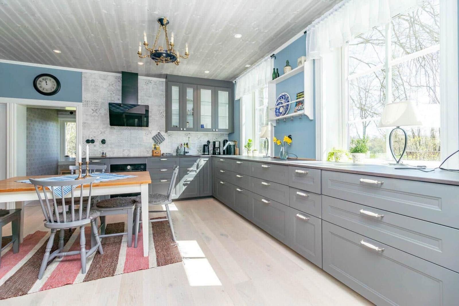 Küche mit grauen Schränken, Essbereich und großem Fenster. Holzboden und Deckenleuchte.