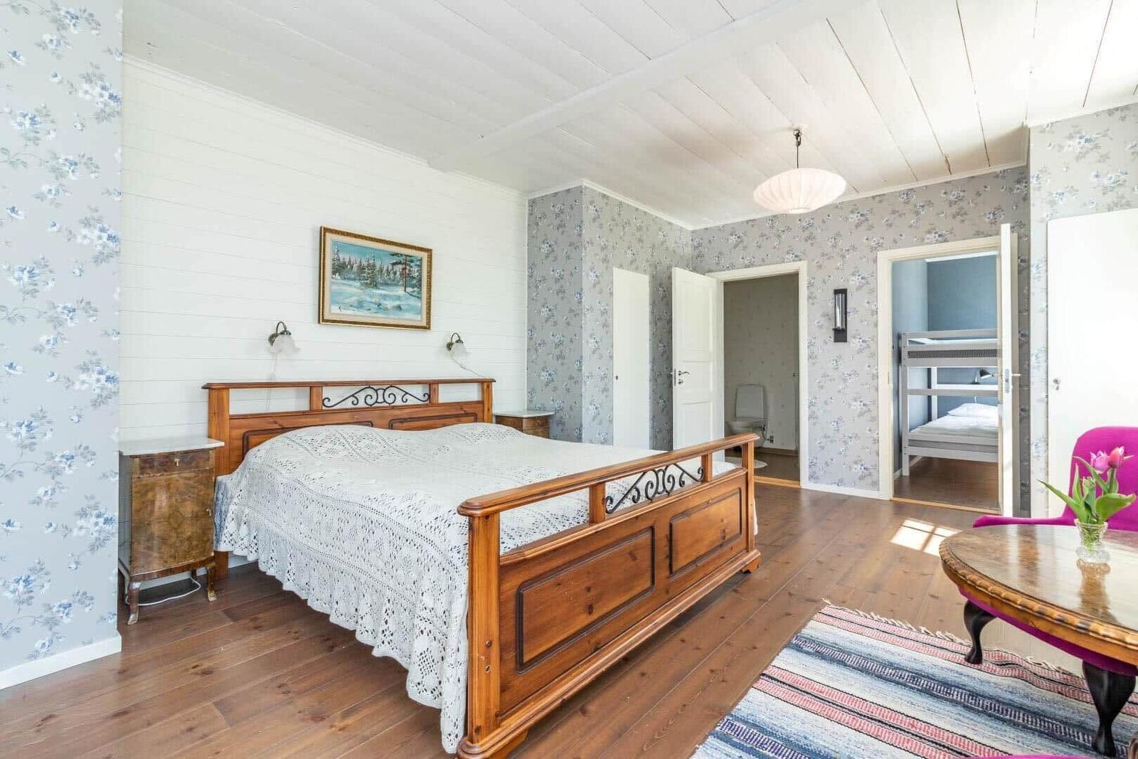 Haupt Schlafzimmer mit Holzbett, Tapete und Blick in Nebenraum mit Schlafcouch.