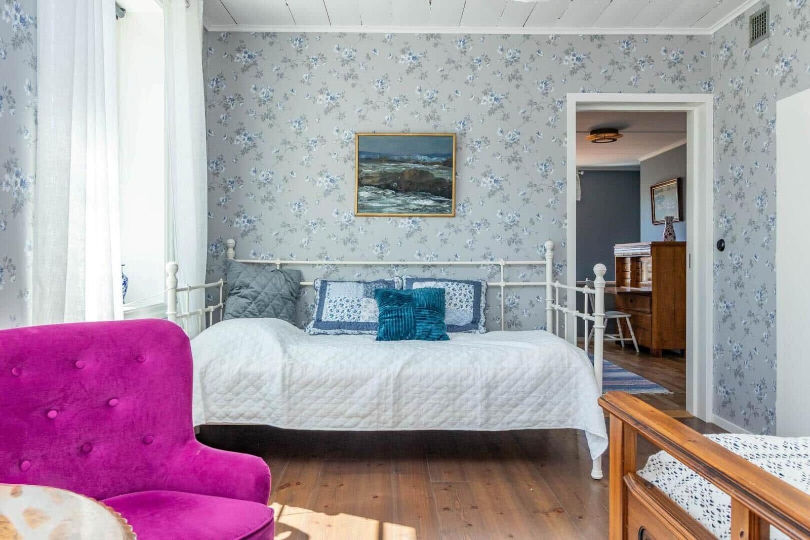 Schlafzimmer mit Bett, pinkem Sessel und floraler Tapete.