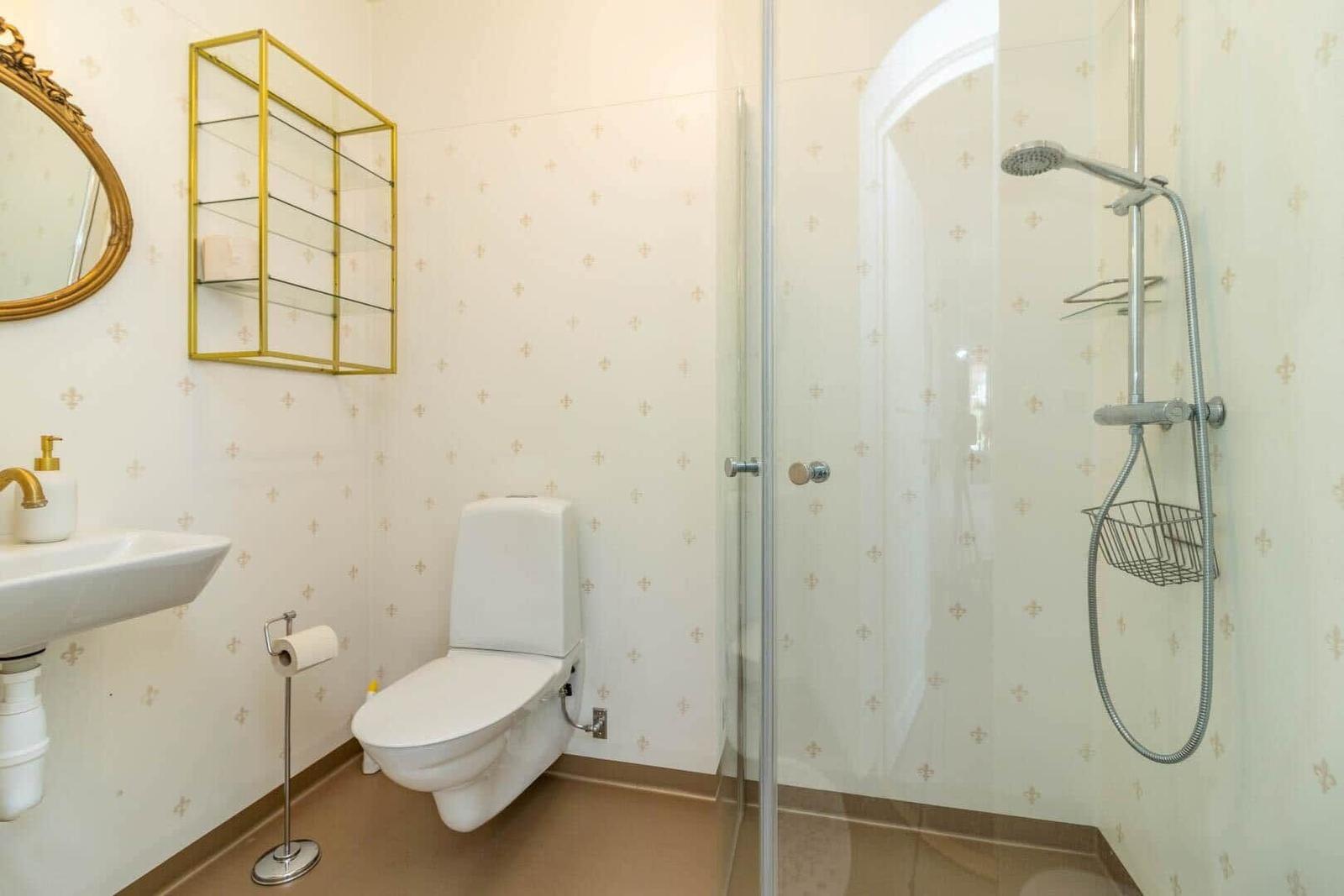 Badezimmer mit Dusche, WC und Waschbecken mit goldfarbenen Akzenten.
