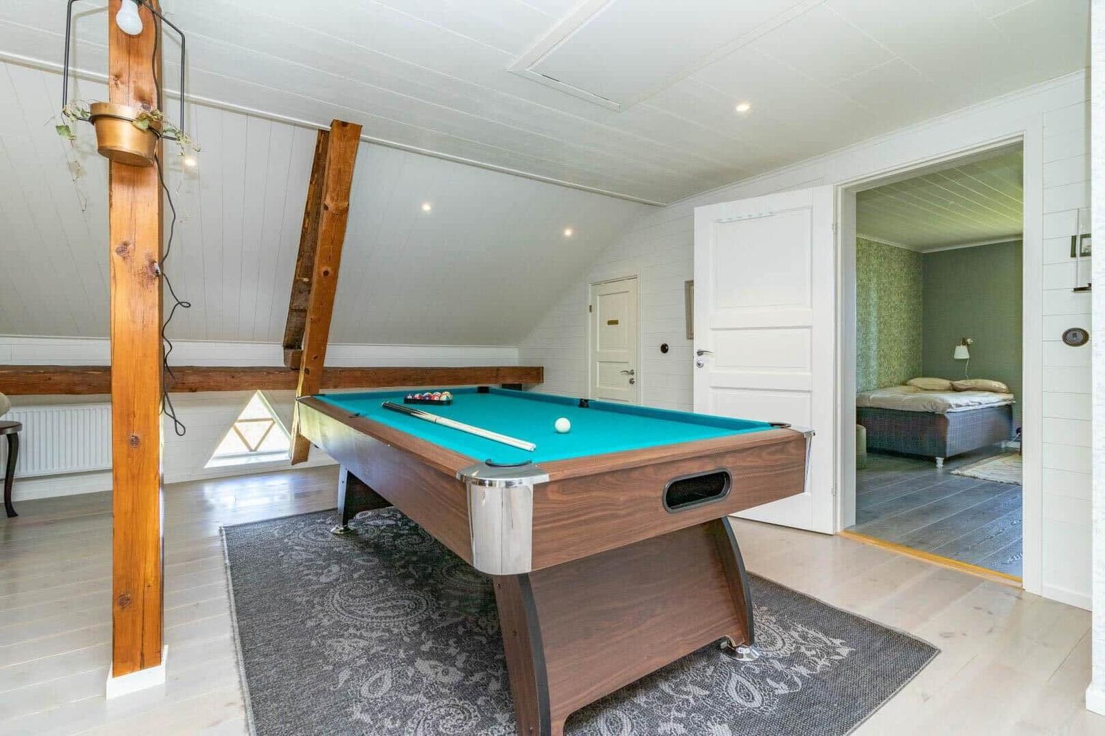 Schlafzimmer mit Bett und Tür. Im Vordergrund befindet sich ein Billardtisch mit grünem Tuch.