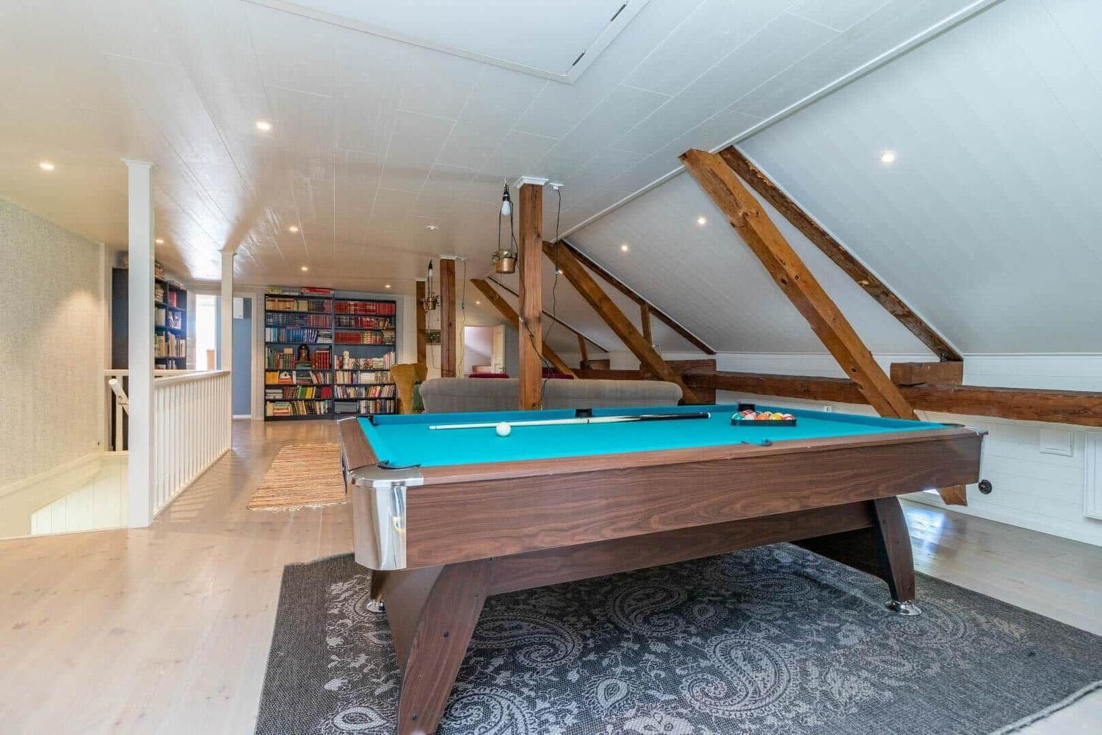 Pooltisch mit blauem Filz in einem Raum mit Holzbalken und Bücherregal im Hintergrund.