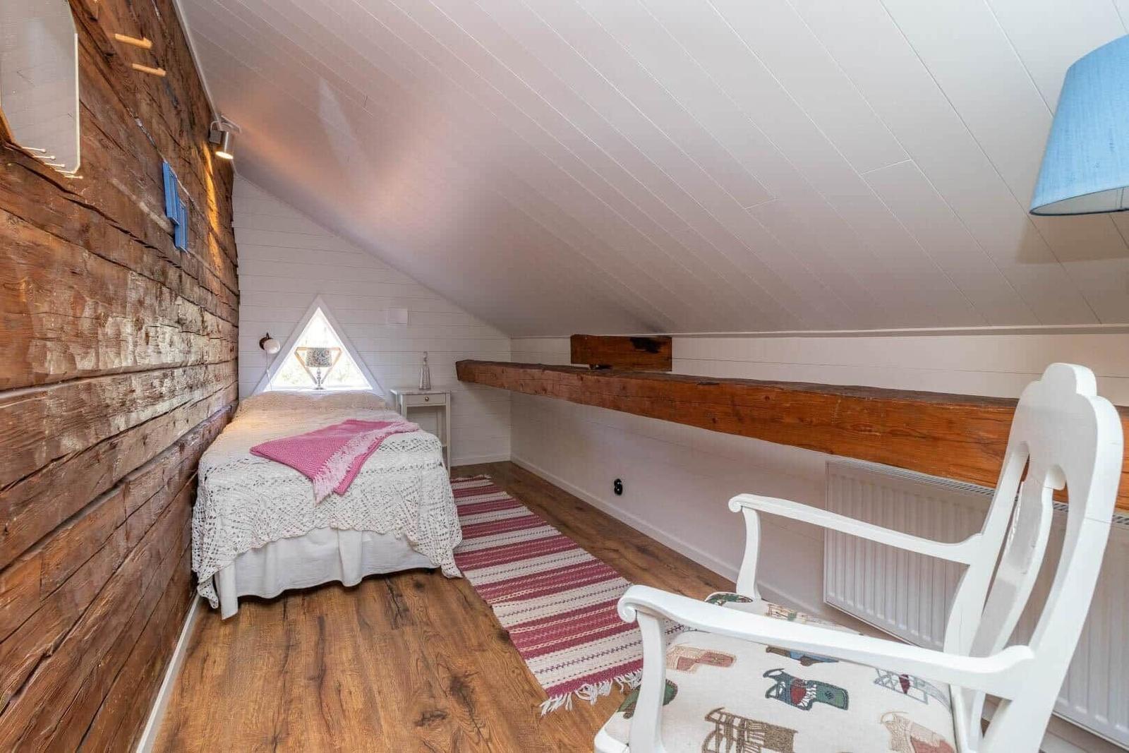 Schlafzimmer mit Holzwand, Bett, Stuhl und Dachschräge.