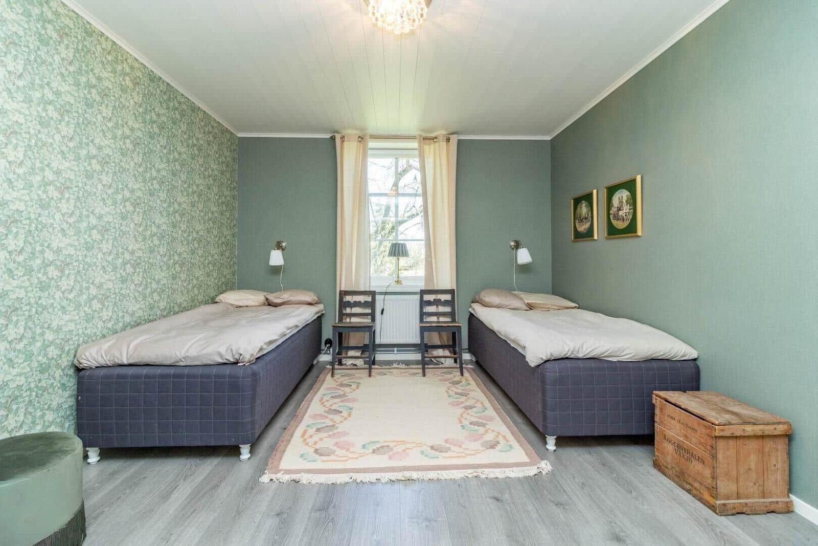 Zwei Betten, ein Fenster, zwei Stühle, Teppich und Holzkiste.