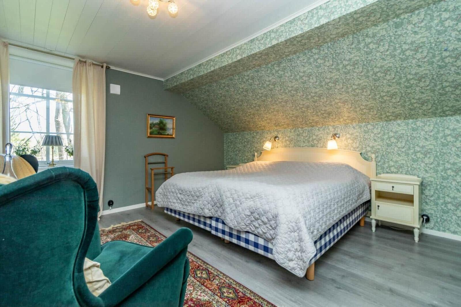 Schlafzimmer mit Bett, Nachttisch, Fenster und grünem Sessel.